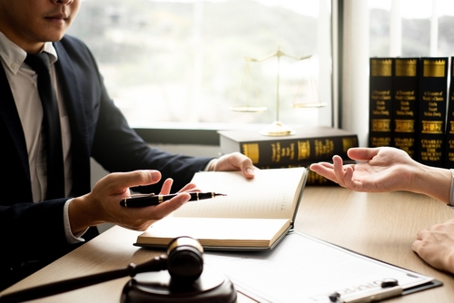 Criminal defense lawyer in a formal suit discusses legal strategy with a client at a desk in a law office.