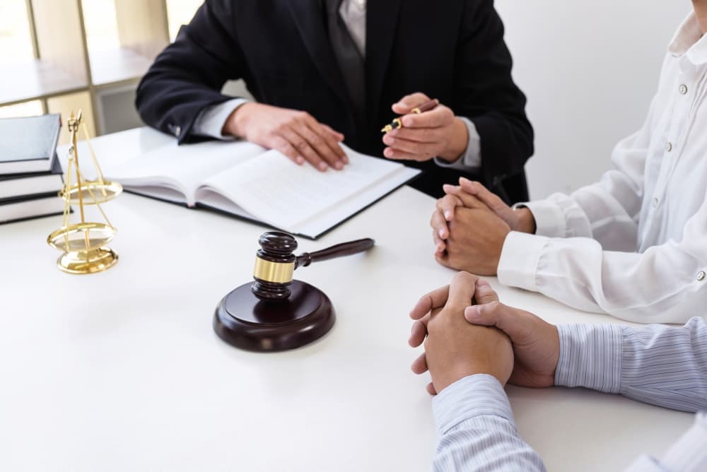 Close-up of a gavel: a male lawyer or judge consults with a client and reviews law books and case reports on the table in a modern office, symbolizing the concept of law and justice.