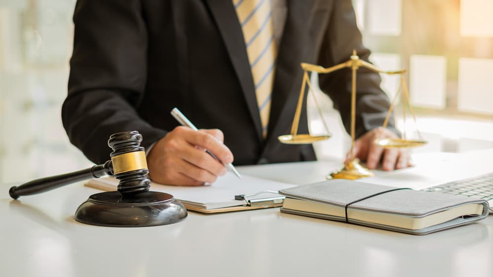 Male attorney or legal advisor meeting with clients in an office setting—featuring legal concepts, a gavel, and justice scales on the desk.