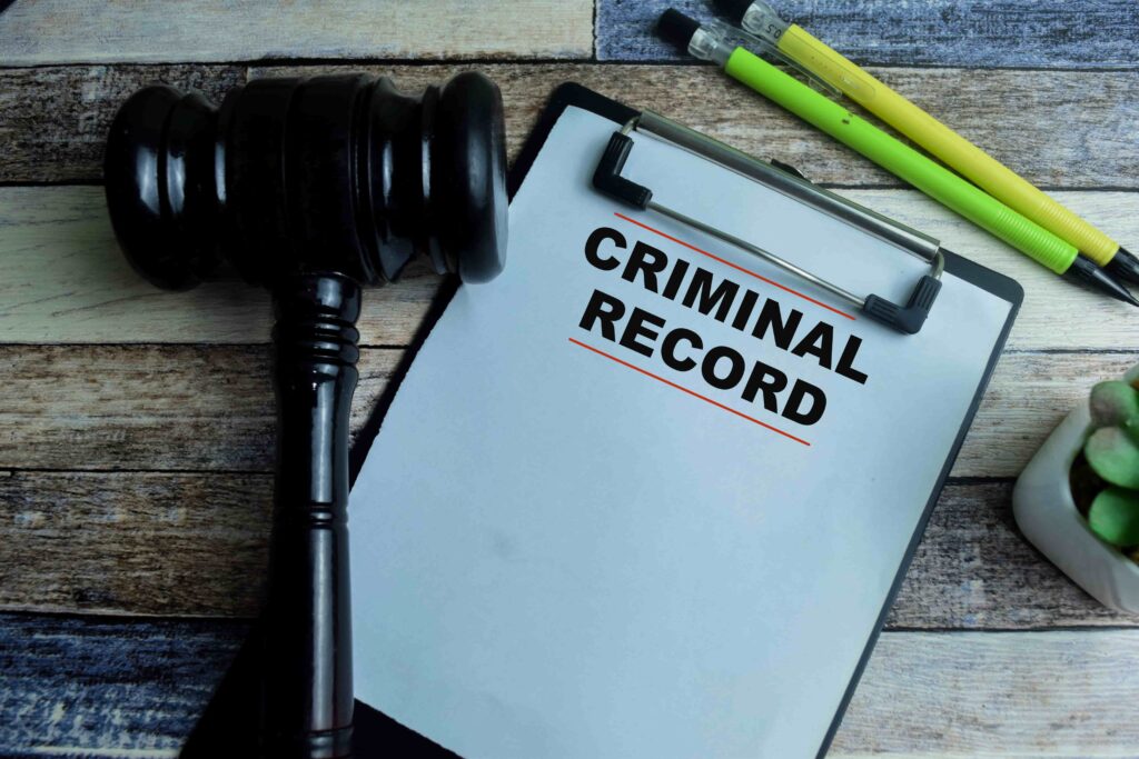 Judge’s gavel beside clipboard with criminal record document on wooden desk
