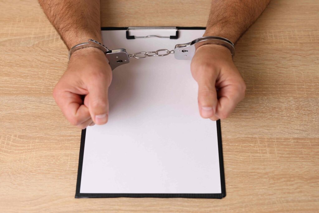 Hands in handcuffs resting on a clipboard, symbolizing arrest, criminal charges, or legal proceedings.